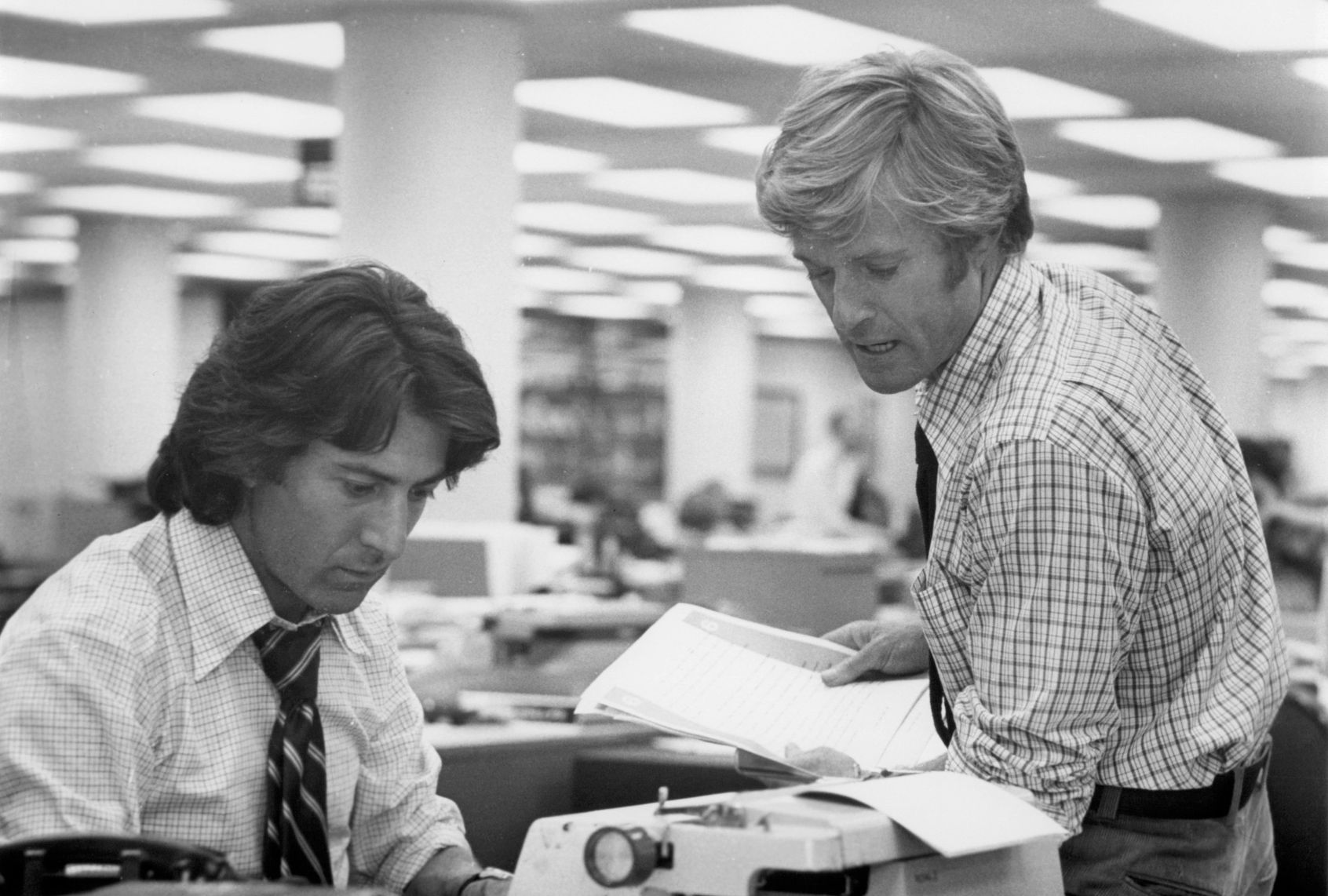 Black and white photo of two men in the newsroom looking down at a typewriter