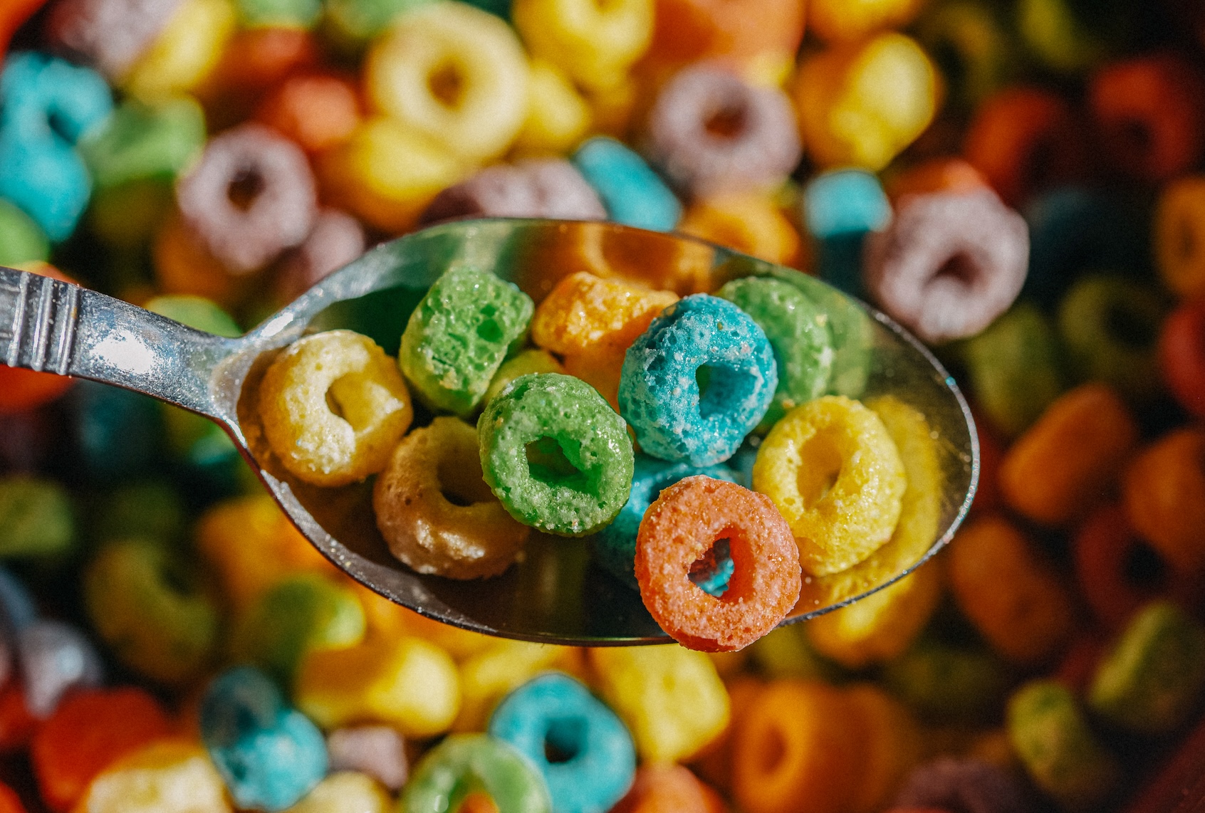 A close-up of a spoon filled with colorful, loop-shaped cereal is surrounded by more vibrant cereal pieces. (Getty Images / Stefania Pelfini, La Waziya Photography)