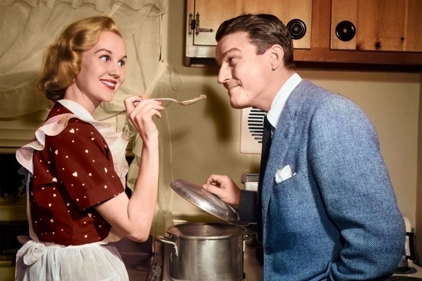 1950s smiling housewife at stove giving happy husband a taste of her cooking (Getty Images/Debrocke/ClassicStock)