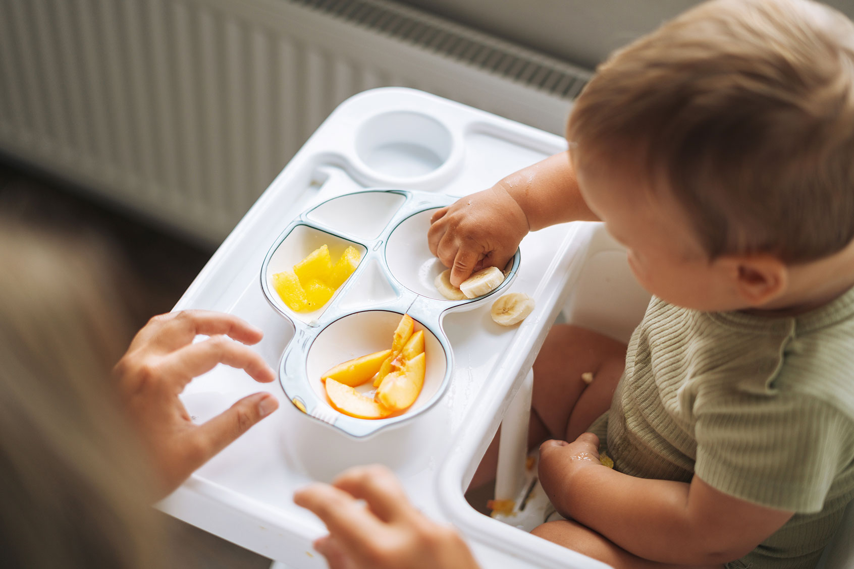 Young mother feeding her baby fruits in a high chair (Getty Images/Galina Zhigalova)